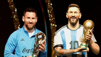 Messi, with the World Cup trophy, next to a statue of the player.