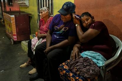 Three people wait for a detained family member in front of El Penalito headquarters in San Salvador.
