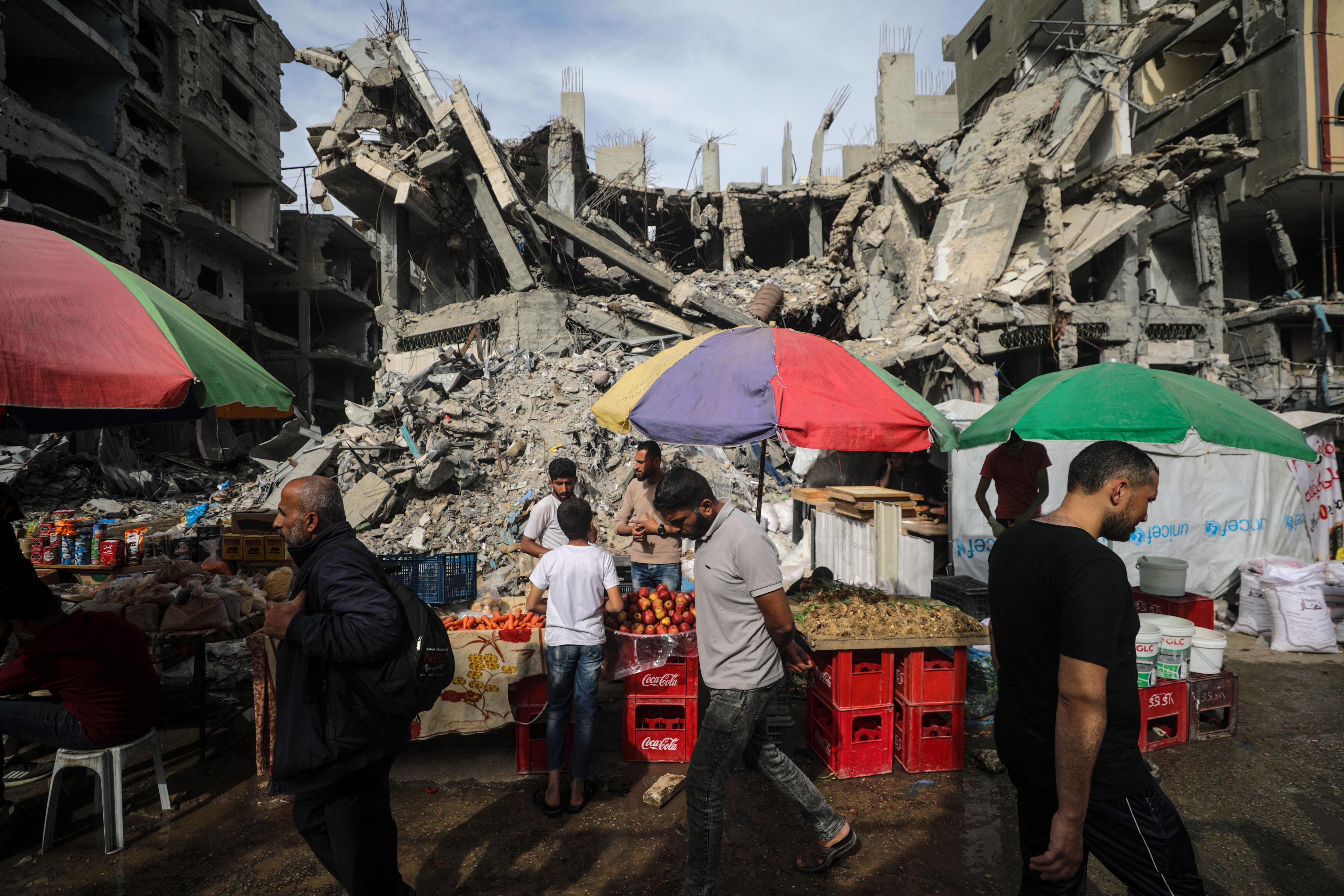 Palestinian men walk past kiosks set up next to buildings of the Nuseirat refugee camp in the Gaza Strip, on April 5, the last Friday of Ramadan.