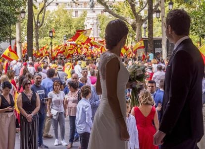 Newlyweds in Seville observe the scene as thousands of people take to the city streets with Spanish flags to call for a united Spain.