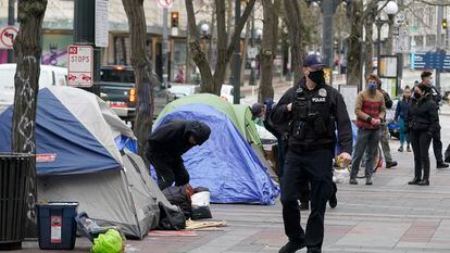 A Seattle police officer walks past tents used by people experiencing homelessness, March 11, 2022, during the clearing and removal an encampment in Westlake Park in downtown Seattle.
