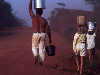 A father walks with his daughters carrying buckets of water along the Transamazon Highway, in Brazil.