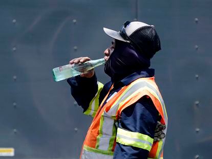 Standing in the mid afternoon heat, a worker takes a break to drink during a parking lot asphalt resurfacing job in Richardson, Texas, Tuesday, June 20, 2023.