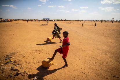 Un niño lleva un bidón de agua, haciéndolo rodar con sus pies descalzos por el suelo seco del campo para desplazados de Ladan, en Dolow.