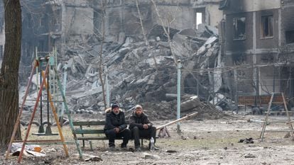 Local residents sit on a bench near an apartment building destroyed in Mariupol.