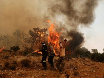 Men help a firefighter as they try to extinguish a wildfire burning near the village Vlyhada, near Athens, Greece, on July 19, 2023.