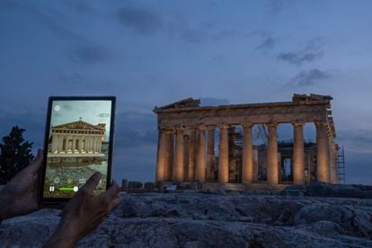 A man holds up a tablet showing a digitally overlayed virtual reconstruction of the ancient Parthenon temple, at the Acropolis Hill in Athens, Greece on Tuesday, June 13, 2023.