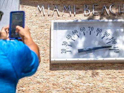A person takes a photo of a Miami Beach Clock Thermometer that marks the temperature at 105 degrees Fahrenheit (about 40 Celsius) during the hottest summer in modern history, in Miami Beach, Florida.