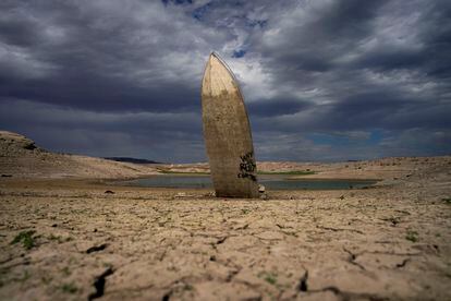 A formerly sunken boat stands upright into the air with its stern buried in the mud along the shoreline of Lake Mead.