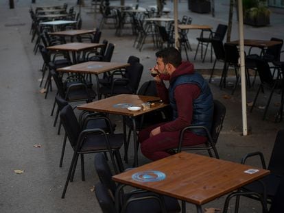 A customer sits at an empty sidewalk café in Barcelona, where new restrictions on the food service industry will come into effect on Monday.