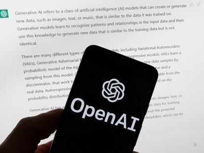 The OpenAI logo is seen on a mobile phone in front of a computer screen displaying output from ChatGPT, March 21, 2023, in Boston