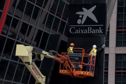 Workers putting up a CaixaBank sign at Bankia headquarters in Madrid's Puerta de Europa towers following the merger.