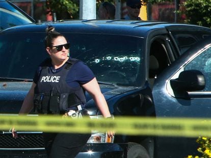 A police officer walks next to a car with bullet holes on the windows at a crime scene in Langley, Canada.