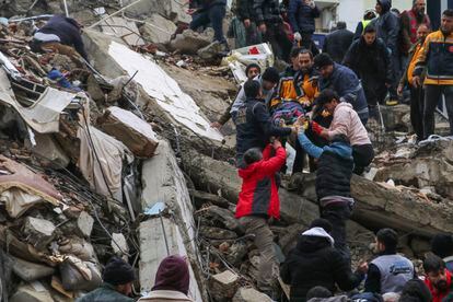 People and emergency teams rescue a person on a stretcher from a collapsed building in Adana, Turkey.