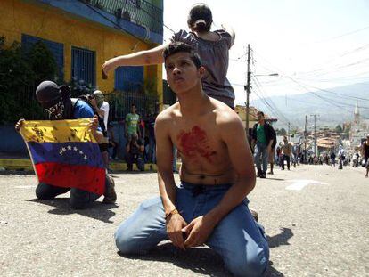 A boy with blood on his chest kneels in front of police after a student died during a protest in San Cristóbal.