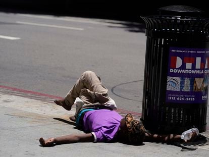 A homeless person lies on the sidewalk while holding a water bottle, Sunday, July 2, 2023
