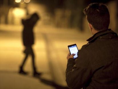 A man checks his cellphone as a young woman walks by.