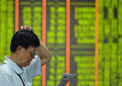 An investor reads in front of a board of share prices in China. Falls are shown in green.