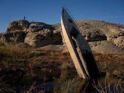 A man stands on a hill overlooking a formerly sunken boat standing upright into the air with its stern buried in the mud along the shoreline of Lake Mead at the Lake Mead National Recreation Area, Friday, Jan. 27, 2023, near Boulder City, Nev.