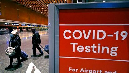 Two travelers pass a COVID testing sign in Boston’s Logan Airport.