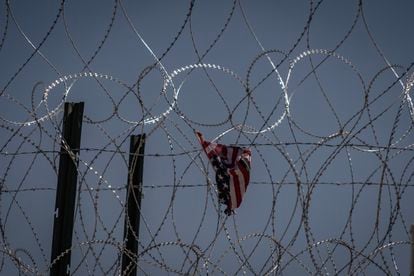 A U.S. flag hangs on a barbed wire fence.