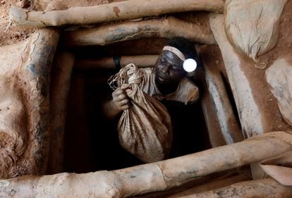 A miner emerges from an unlicensed gold mining pit with bags of broken rock, in Nsuaem Top, Ghana; November 2018.