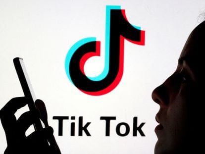 A person holds a mobile in front of the TikTok logo.
