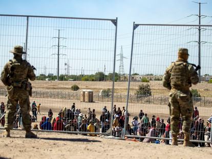 Migrants wait in line adjacent to the border fence under the watch of the Texas National Guard to enter into El Paso, Texas, on May 10, 2023.