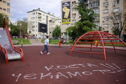 A boy walks past graffiti on a playground that reads "Kosta we are waiting for you," in Belgrade, Serbia, on May 6, 2023.