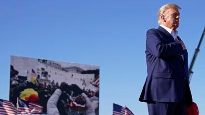FILE - As footage from the Jan. 6, 2021, insurrection at the U.S. Capitol is displayed in the background, former President Donald Trump stands while a song, "Justice for All," is played during a campaign rally at Waco Regional Airport, Saturday, March 25, 2023, in Waco, Texas. The tune, “Justice for All,” is the Star-Spangled Banner and it was sung by a group of defendants jailed over their alleged roles in the January 2021 insurrection. The national anthem is overlaid with Trump reciting the Pledge of Allegiance. (AP Photo/Evan Vucci, File)