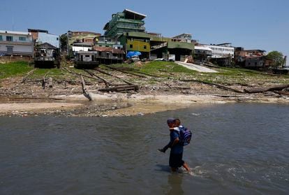 A man carries his son across the Rio Negro to take him to school, on September 26, 2023. Manaus – the state capital – is in an emergency situation. The drought is expected to reach its peak in the second half of October, according to the Geological Survey of Brazil.