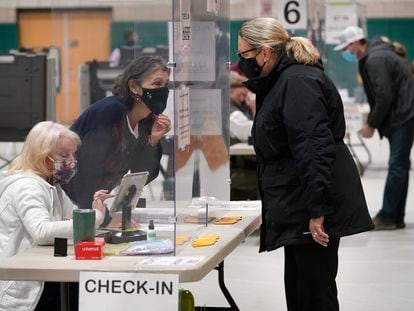 A poll worker, center left, speaks through a plastic barrier while assisting a voter in a polling station at Marshfield High School, Nov. 3, 2020, in Massachusetts.