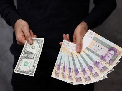 A currency dealer poses for a photo with a U.S one dollar bill and the amount being given when converting it into Iranian rials in an exchange shop in Tehran, Iran December 25, 2022.