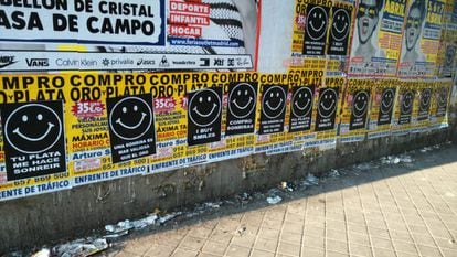 Posters advertising “I buy gold” covered with signs saying “I buy smiles” and “A smile is more valuable than gold.”