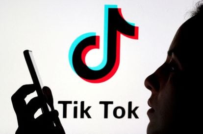 A person holds a mobile in front of the TikTok logo.