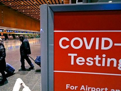Two travelers pass a COVID testing sign in Boston’s Logan Airport.