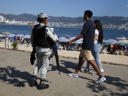 People walk by a member of the National Guard as she keeps watch at Papagayo beach during Holy Week in Acapulco.