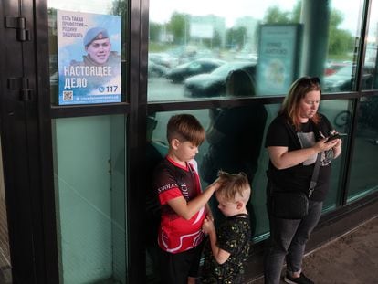 A woman and her children at a shopping center in Smolensk stand by a sign urging Russians to enlist; August 22, 2023.