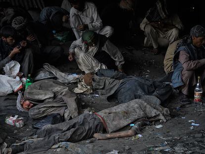 The body of a drug addict lies under Kabul's Pul-e-Sukhta Bridge while his colleagues continue to use drugs.