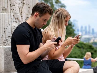Two people use their cell phones in a public space.