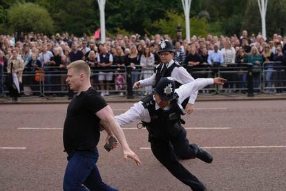 Police officers chase a man who jumped a barrier moments before Charles III's car arrived at Buckingham Palace. 