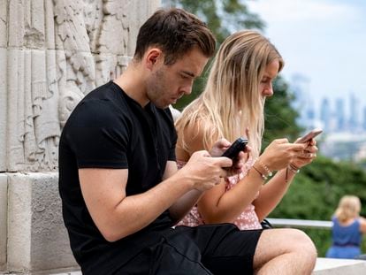 Two people use their cell phones in a public space.