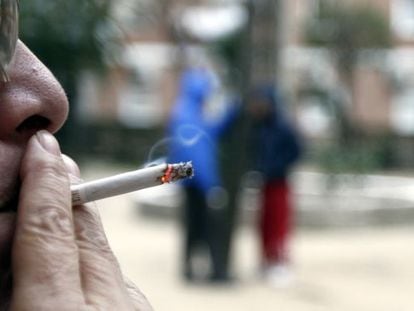 A woman smokes a cigarette in a park.