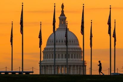 An early morning pedestrian is silhouetted against sunrise as he walks through the American flags on the National Mall with the U..S Capitol Building