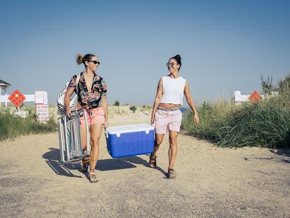 Two women carry a cooler to the beach.