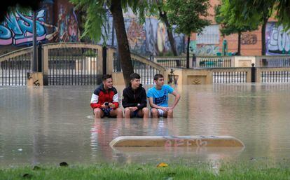 Three youngsters sit on a bench in a flooded park in Orihuela.