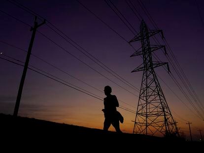 A jogger passes power lines during a sunset run, Aug. 20, 2023, in San Antonio, as high temperatures continue to stress the power grid.
