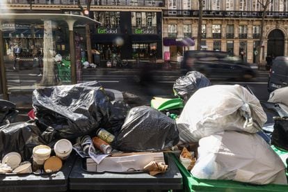People pass by next to garbage cans overflowing with trash in Paris, France, 14 March 2023. Garbage collectors have joined the massive strikes in France against the government's pension reform plans, piling the streets of the French capital in the meantime with thousands of tons of garbage. 