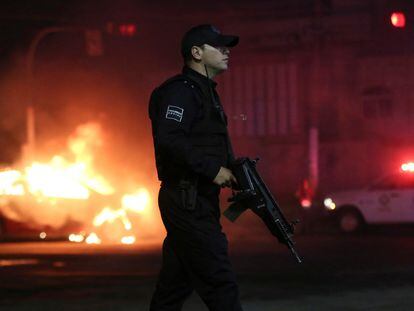 A police officer stands near a vehicle set on fire by members of Jalisco New Generation Cartel.