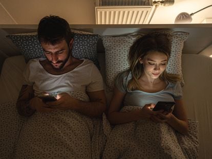 A couple looking at their mobile phones in bed.